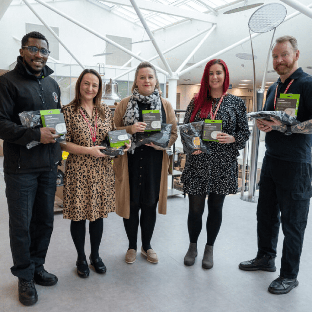Five people indoors smiling, holding awards and Winter Warmth pack donations.