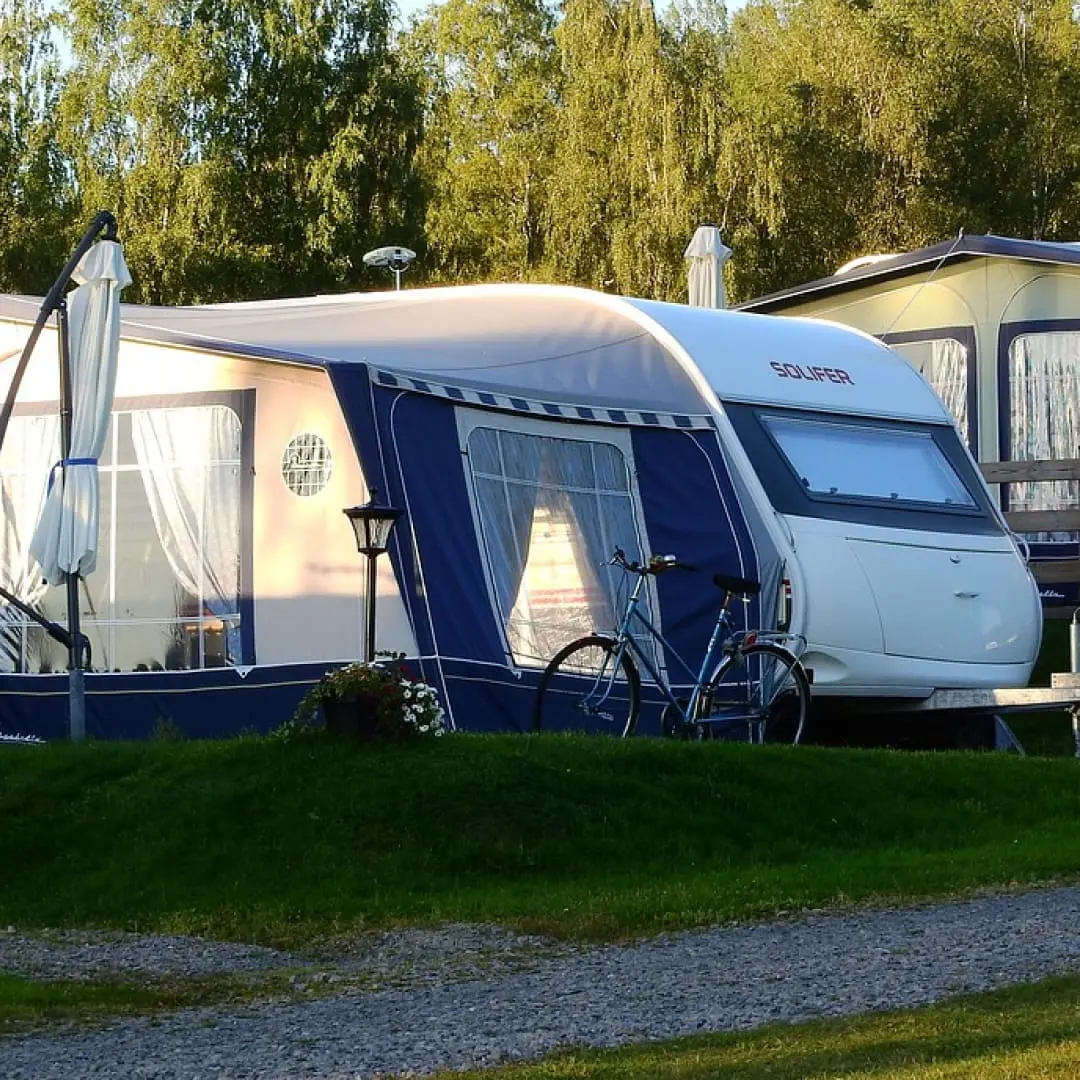 A white and blue campervan with awning, bicycle, and leisure vehicle safety features on green grass.