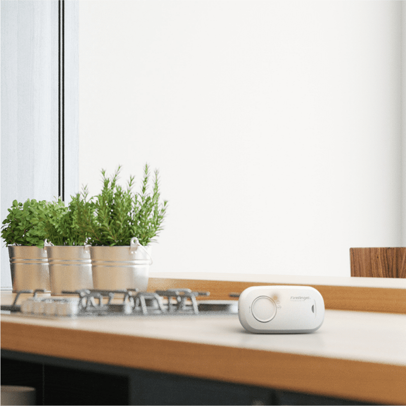 White gas detector with alarm memory on a kitchen worktop beside herbs and a hob.