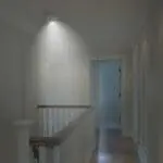 The FA6611-R smoke detector emits light on a hallway ceiling near the stairs and open door.