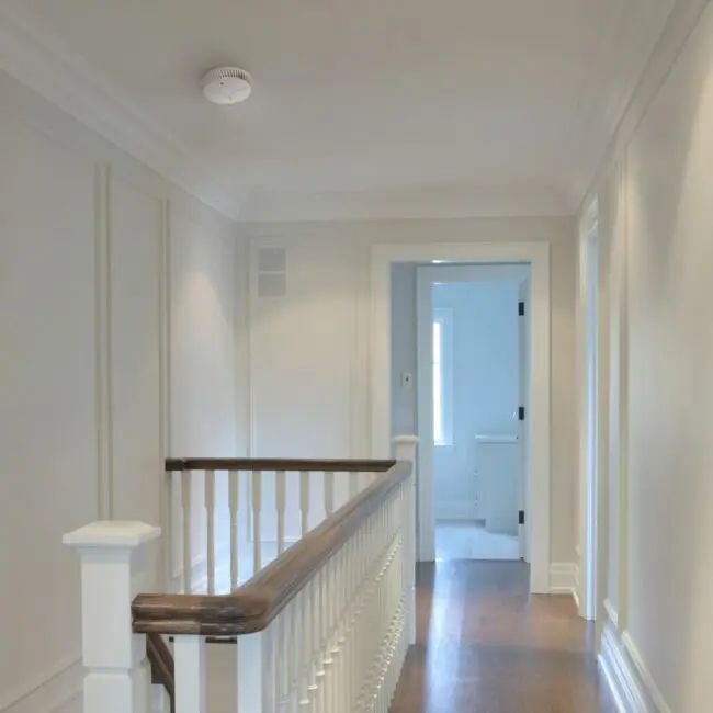 Bright corridor with white walls, wooden handrail, and FA6615-R doorway leading to a bathroom.