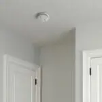 FA6620-R smoke detector on a white ceiling near two white door frames in a corner.