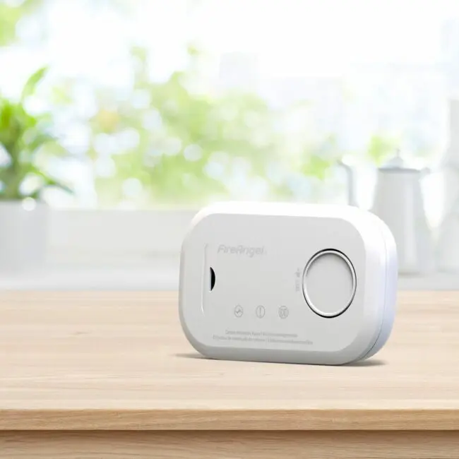FA6813 carbon monoxide detector on wooden surface with blurred kitchen background.