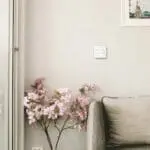 Pink flowers in vase beside grey sofa and FP1014W2-R switch on beige wall.