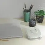 A desk with a notebook, pencils in a cup, a candle, a plant, and an FP1820W2-R.