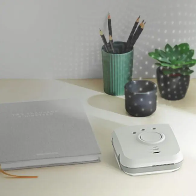 A desk with a notebook, pencils in a cup, a candle, a plant, and an FP1820W2-R.