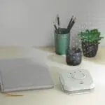 A desk with a notebook, FS1326-T, pencils in a pot, small plant, and candle.