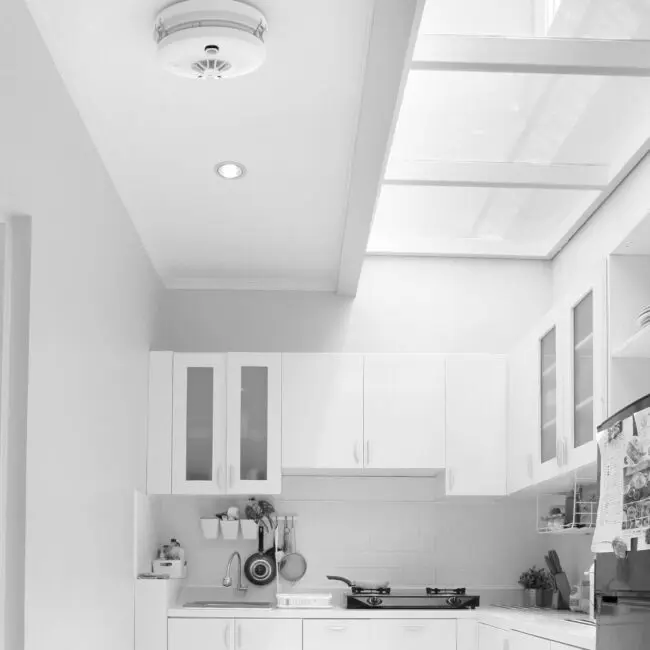 Modern white kitchen featuring HW1-PF-T smoke detector on ceiling with skylights above.