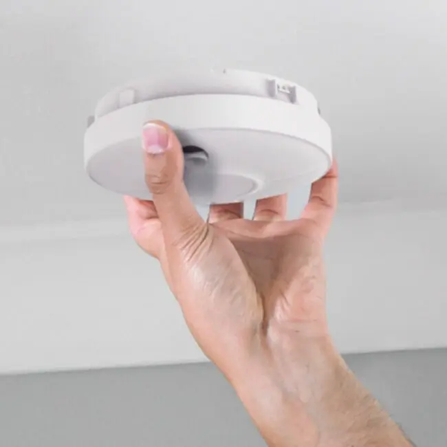 Hand installing SW10-EUT smoke detector onto a white ceiling.