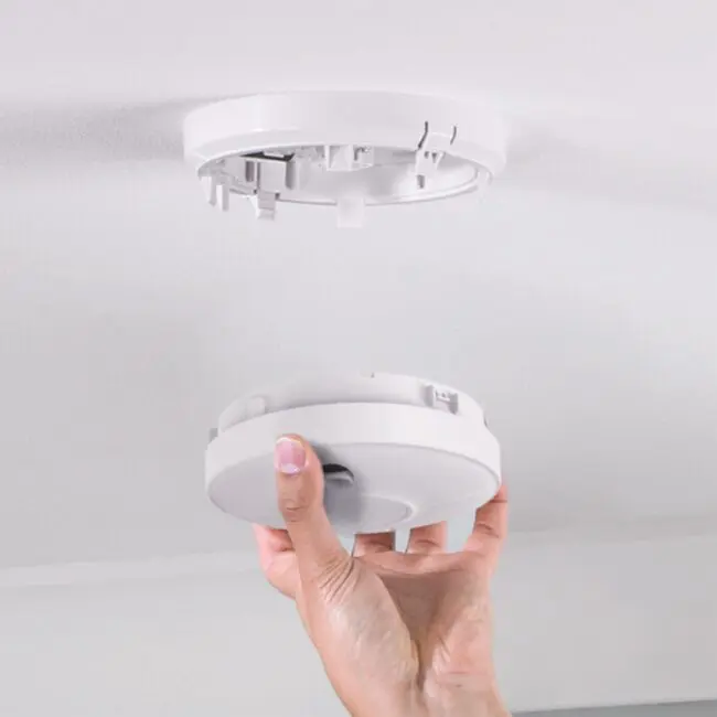 A hand installs or removes a CW1-PF-T smoke detector from a ceiling mount.