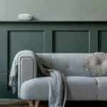 Light grey FA3820X4 sofa with round cushion and blanket, under a speaker on a green wall.