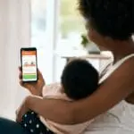 Woman with baby checks health tracking info on FP1000W2-R smartphone app.