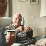 Elderly couple chats in cosy room, mugs in hand by FP1014W2-R smart control switch.