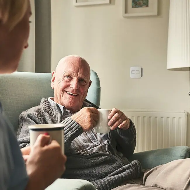 Elderly couple chats in cosy room, mugs in hand by FP1014W2-R smart control switch.