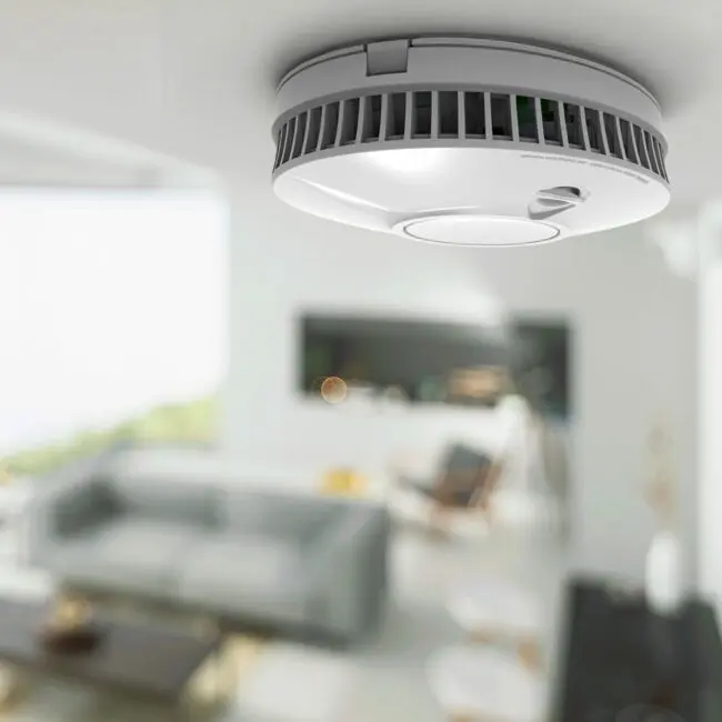 FP1640W2-R smoke detector mounted on ceiling in a modern living room, close-up.
