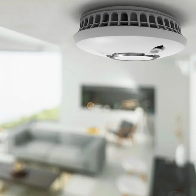 The FP2620W2-R smoke detector is mounted on a ceiling in a modern lounge.