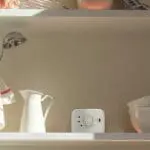A white FS1326-T carbon monoxide detector sits on a kitchen shelf near crockery and a jug.