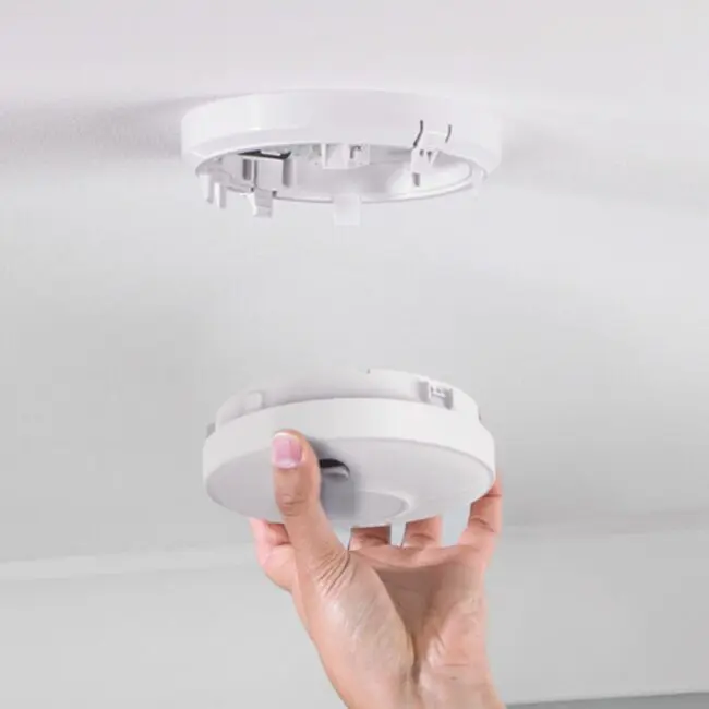 Hand installing or removing an RF-BW-T smoke detector from a ceiling mount.
