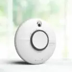 A white SCB10-R smoke and CO alarm on a light surface with a blurred background.