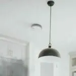 An SW1-R smoke detector with a black pendant light on a white kitchen ceiling.