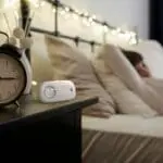 A person relaxing in bed with an FA3313x4 clock and air monitor on the bedside table.