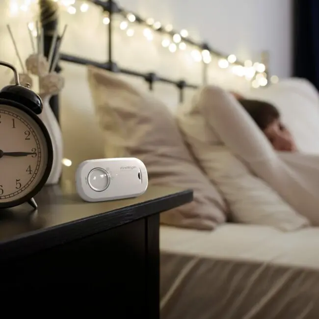 A person relaxing in bed with an FA3313x4 clock and air monitor on the bedside table.