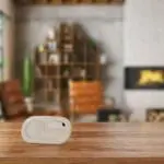 An FA3328-EUT carbon monoxide detector sits on a wooden table in a cosy living room.
