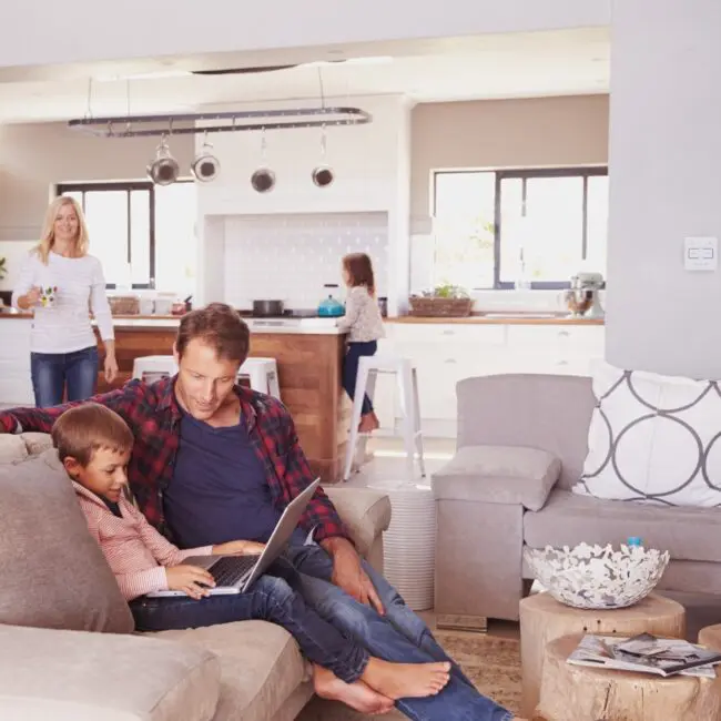 Father and son with laptop; FP1014W2-R smart switch in kitchen with mother and daughter.