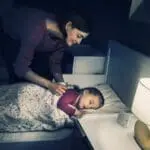 A woman tucks a sleeping child into bed in a softly lit bedroom featuring FS1326-T.