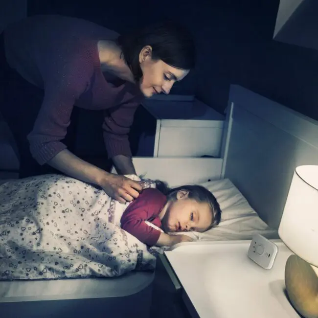 A woman tucks a sleeping child into bed in a softly lit bedroom featuring FS1326-T.