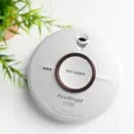 White FireAngel ST-750T smoke alarm with Test/Silence button beside a green plant.