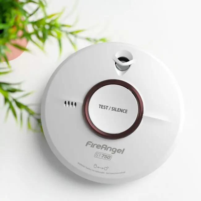White FireAngel ST-750T smoke alarm with Test/Silence button beside a green plant.