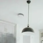 SW10-EUT smoke detector and black hanging pendant light on a white ceiling in a modern room.