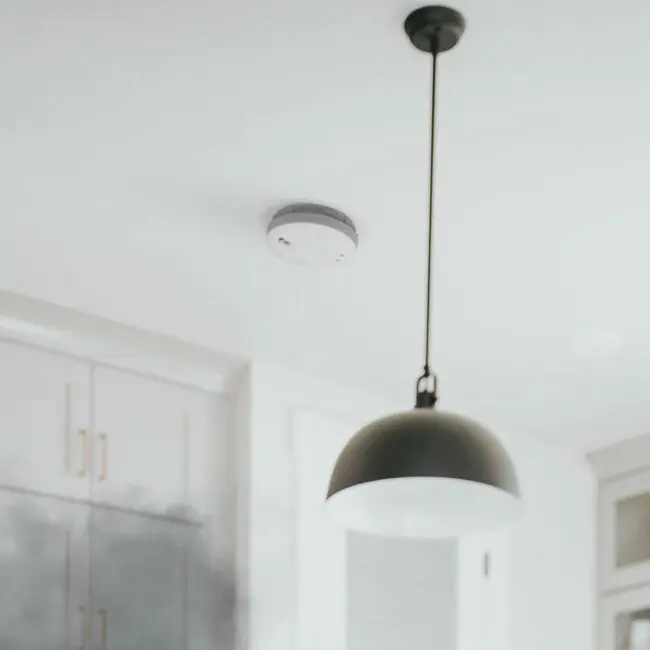 SW10-EUT smoke detector and black hanging pendant light on a white ceiling in a modern room.