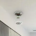 FP1720W2-R smoke detector on ceiling with cover off, showing internal components.