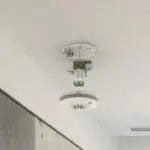 The FP1740W2-R smoke detector is on the ceiling with its cover and inner parts visible.