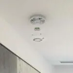 FP2620W2-R smoke detector with cover removed, exposing wiring on a white ceiling.