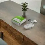 FA3313x4 device, box, and batteries on a wooden table next to a small potted plant.