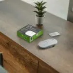 The FA3328-EUT smoke alarm, box, and instructions sit on a wooden table with a plant.