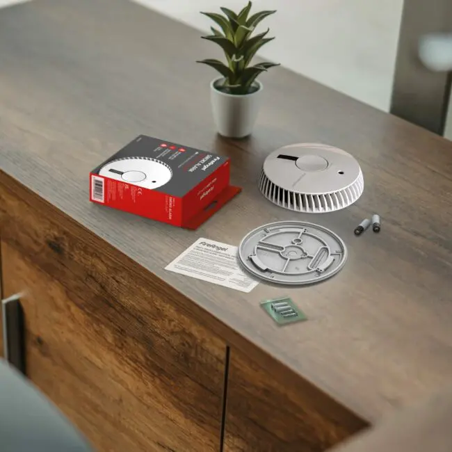 FA6611-R smoke detector kit with parts and instructions on a desk near a small potted plant.