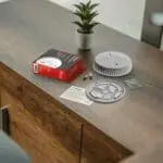 FA6615-R smoke detector kit with parts and instructions on a desk beside a small potted plant.