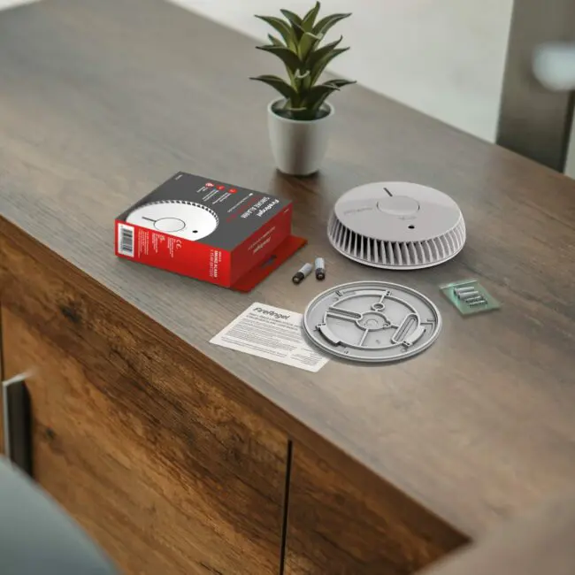 FA6615-R smoke detector kit with parts and instructions on a desk beside a small potted plant.
