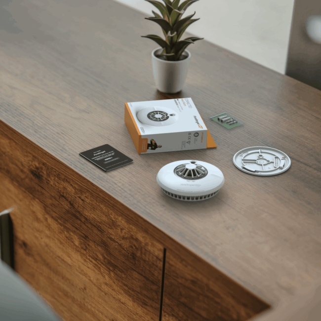 FP1720W2-R smoke detector kit with box and parts on a cupboard next to a potted plant.