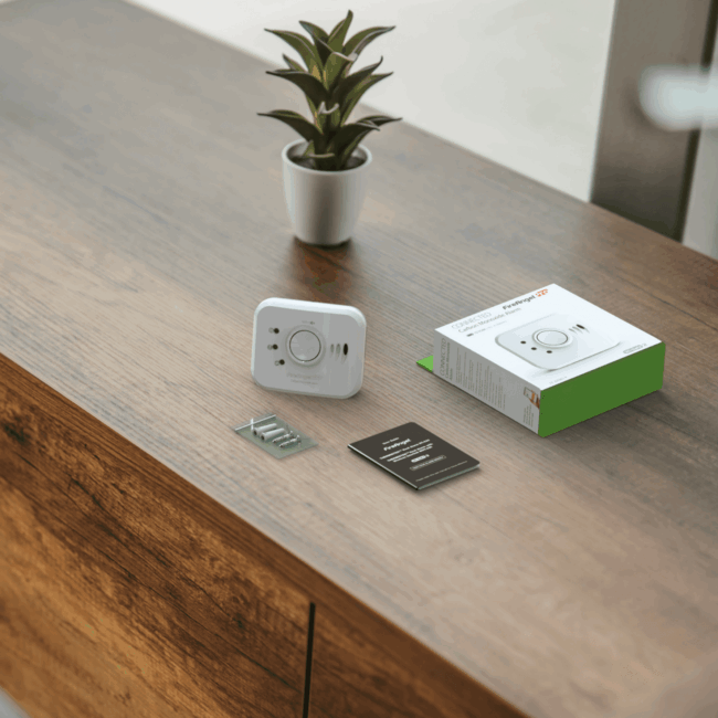 FP1820W2-R alarm, manual, screws, and box on a wooden surface beside a plant.