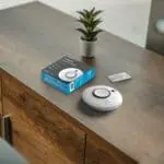 An SCB10-R alarm, its box, and leaflet sit on a cupboard beside a small potted plant.