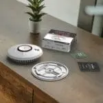 ST-750T smoke alarm, mounting plate, manual, and box on wood beside a potted plant.