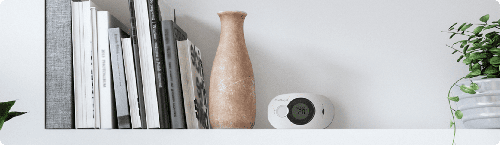 A shelf with books, a tan vase, a digital device, and a Renting Homes regulation booklet.