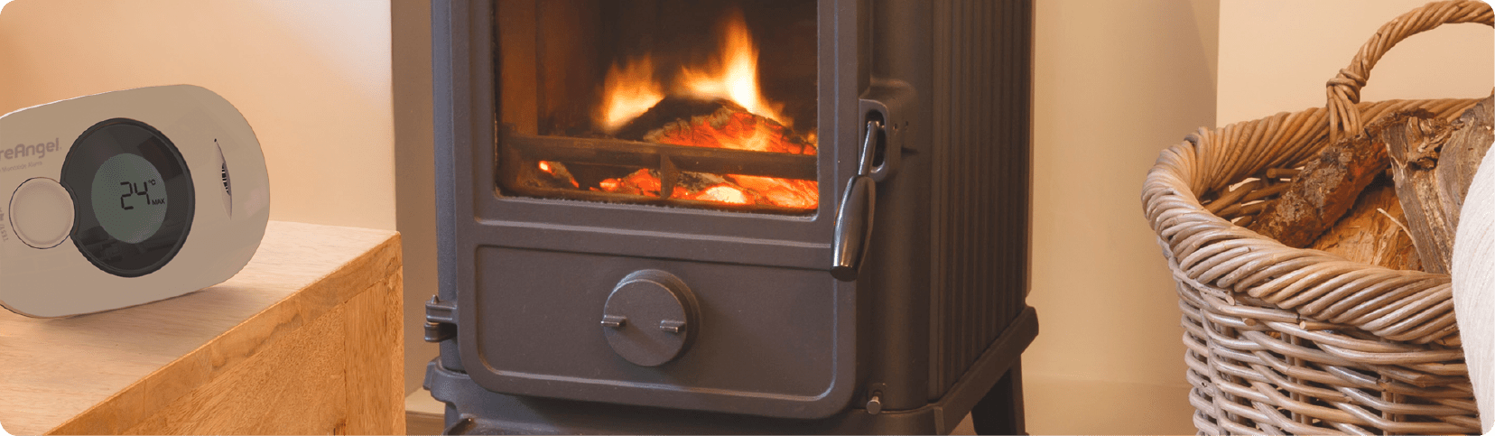 Wood-burning stove near a firewood basket and a BS EN 50292:2023 CO thermometer.