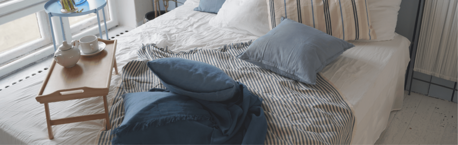 Unmade bed with blue pillows, striped blanket, and tray—ideal for short-term holiday lets.