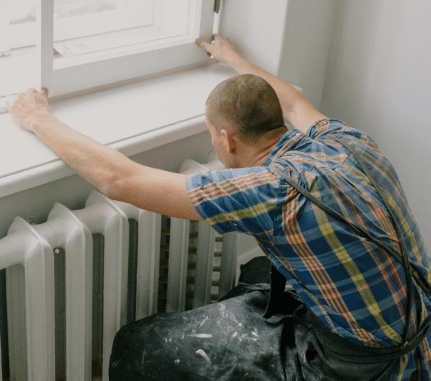 Person adjusts window above radiator, following 2022 Renting Homes Wales Regulations.